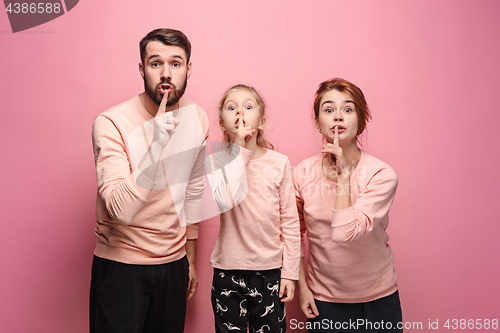 Image of Surprised young family looking at camera on pink