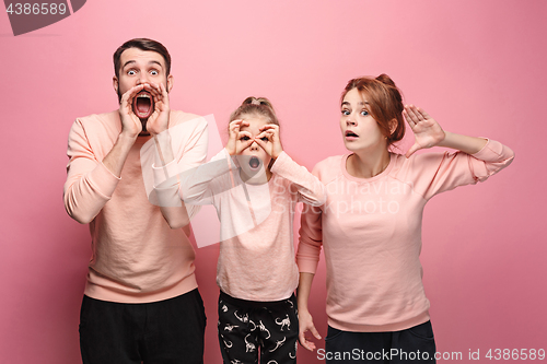 Image of Surprised young family looking at camera on pink