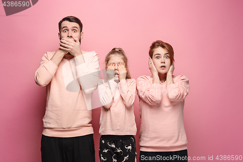 Image of Surprised young family looking at camera on pink