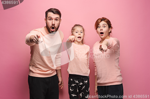 Image of Surprised young family looking at camera on pink