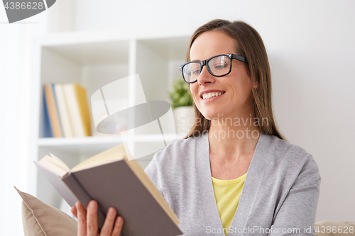 Image of young woman in glasses reading book at home