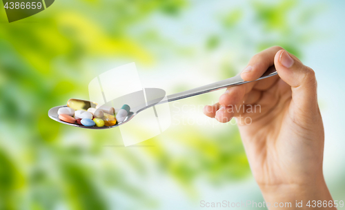 Image of close up of female hand holding spoon with pills