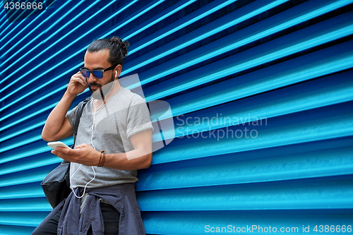 Image of man with earphones and smartphone over wall