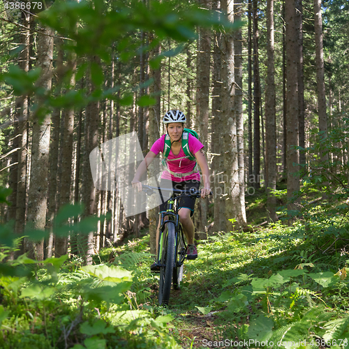 Image of Active sporty woman riding mountain bike on forest trail .