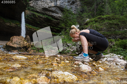 Image of Active sporty woman drinking water from outdoor stream with her hands.