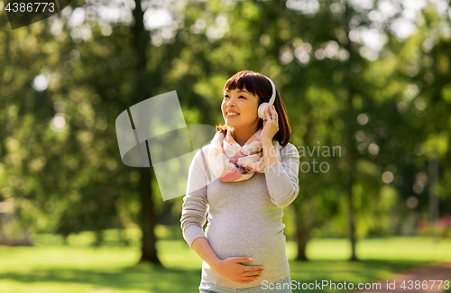 Image of happy pregnant asian woman in headphones at park