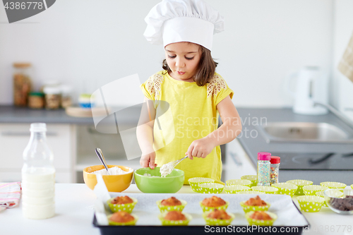 Image of little girl in chefs toque baking muffins at home