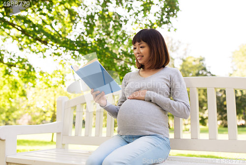 Image of happy pregnant asian woman reading book at park