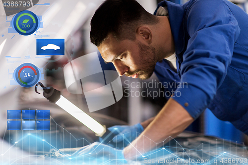 Image of mechanic man with lamp repairing car at workshop