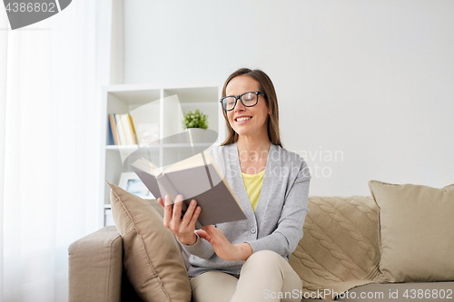 Image of happy woman in glasses reading book at home