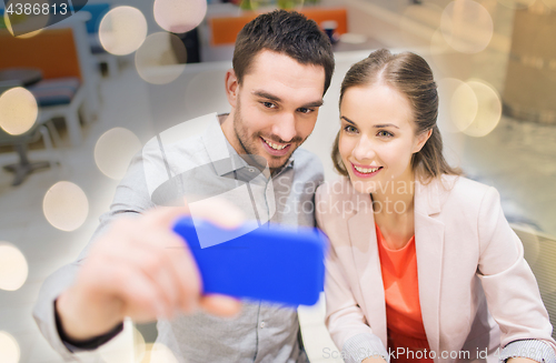 Image of happy couple taking selfie with smartphone in cafe