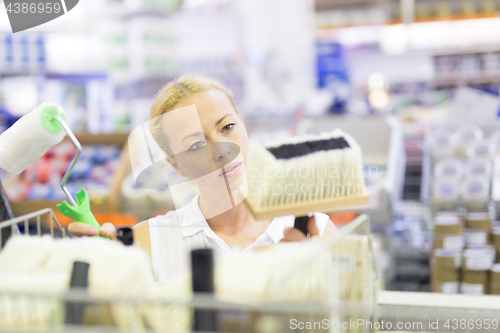 Image of Young independent woman buying tools for house decoration in paint supplies shop.