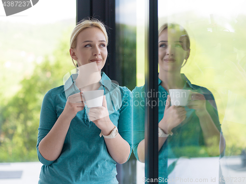 Image of young woman drinking morning coffee by the window