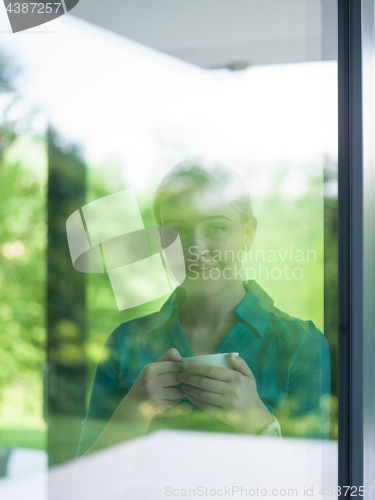 Image of young woman drinking morning coffee by the window