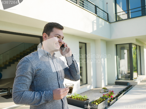 Image of man using mobile phone in front of his luxury home villa