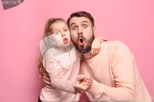 Image of Surprised young family looking at camera on pink