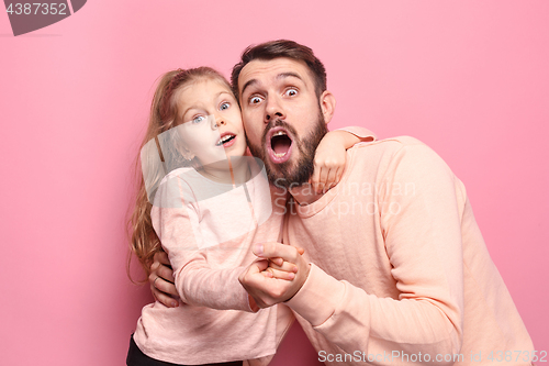 Image of Surprised young family looking at camera on pink