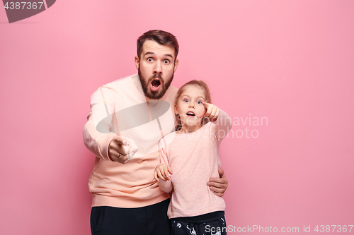 Image of Surprised young family looking at camera on pink