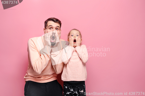 Image of Surprised young family looking at camera on pink