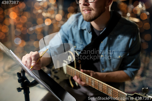 Image of man with guitar writing to music book at studio