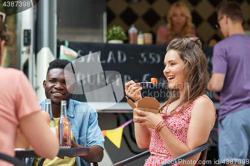 Image of happy friends with drinks eating at food truck