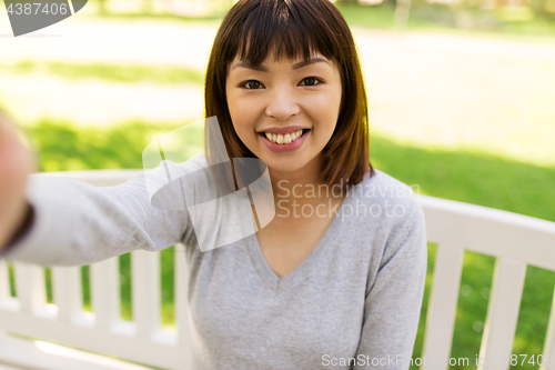 Image of happy smiling asian woman taking selfie at park