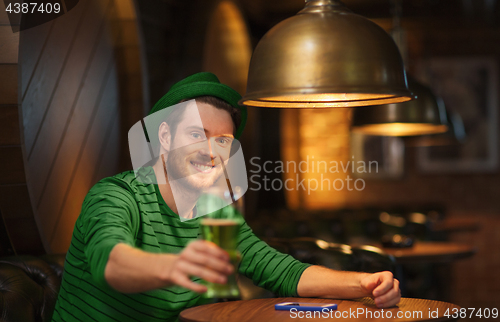 Image of smiling man drinking green beer at bar or pub