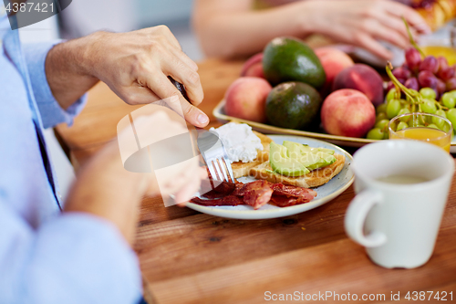 Image of man with fork eating bacon at table full of food