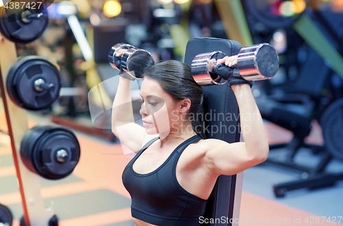 Image of young woman flexing muscles with dumbbell in gym