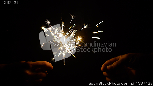 Image of hands holding burning sparklers or bengal lights