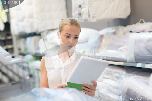 Image of Woman buying bed sheets for her bed in modern home furnishings store.