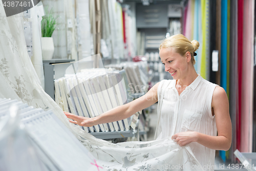 Image of Beautiful housewife buying white curtains in home decor furnishings store.