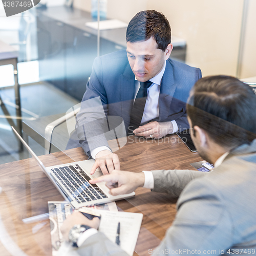 Image of Two young businessmen using laptop computer at business meeting.