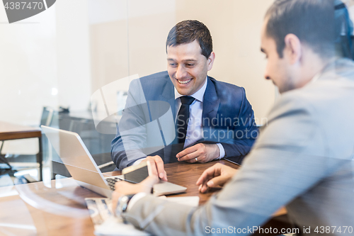 Image of Two young businessmen using laptop computer at business meeting.