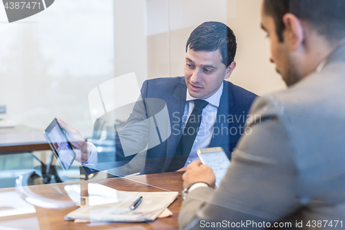 Image of Two young businessmen using electronic devices at business meeting.