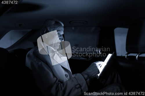 Image of Businessman with a digital tablet sitting in the back seat of a car