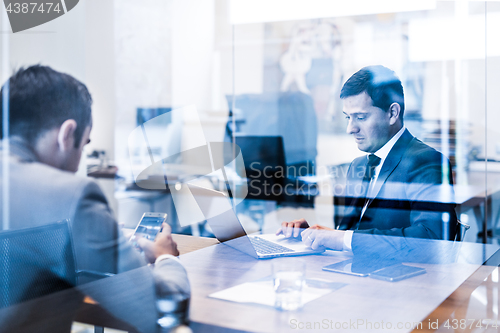 Image of Two young businessmen using laptop computer at business meeting.