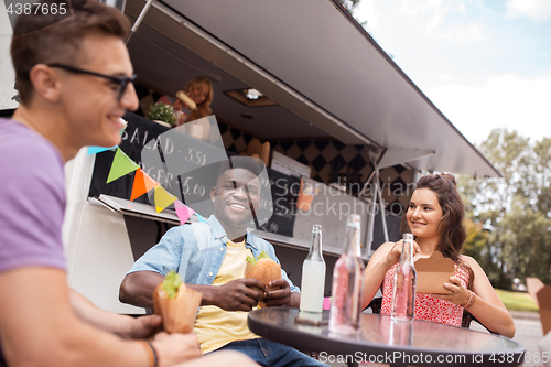 Image of happy friends with drinks eating at food truck