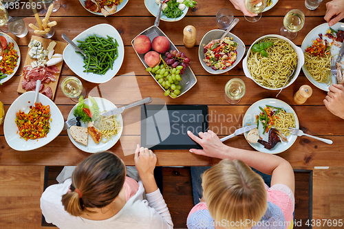 Image of women with tablet pc at table full of food