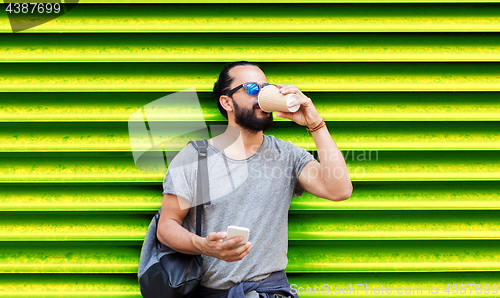 Image of man with smartphone drinking coffee over wall