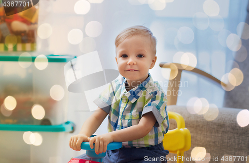 Image of happy little baby boy driving ride-on car at home