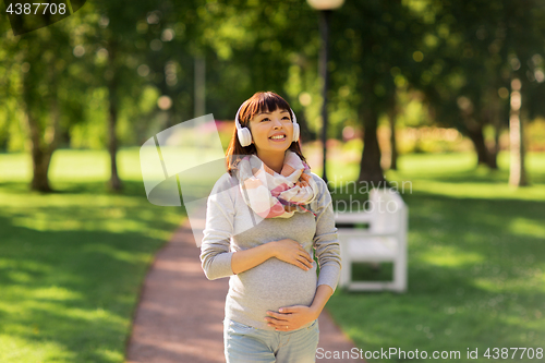 Image of happy pregnant asian woman in headphones at park