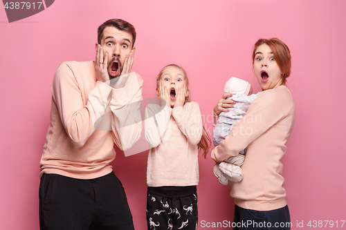 Image of Surprised young family looking at camera on pink