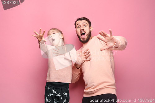 Image of Surprised young family looking at camera on pink