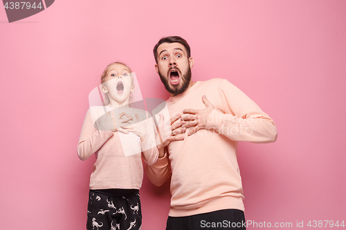 Image of Surprised young family looking at camera on pink