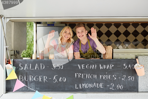 Image of happy couple of sellers waving hands at food truck