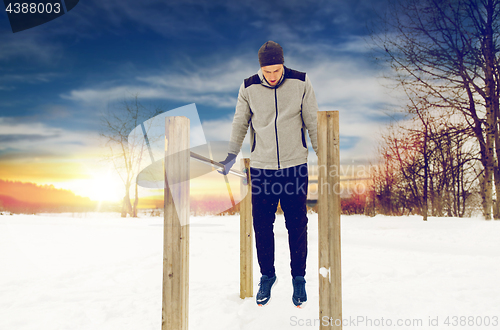 Image of young man exercising on parallel bars in winter