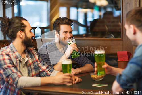 Image of male friends drinking green beer at bar or pub