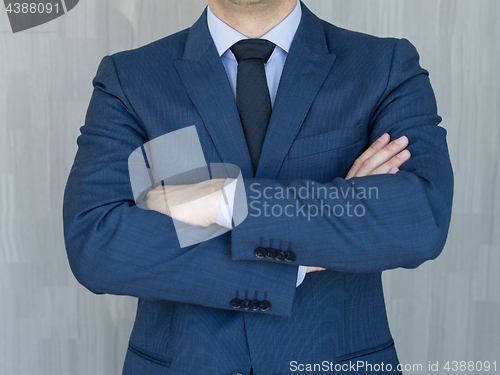 Image of Torso of a businessman standing with folded arms in a classic navy blue suit.