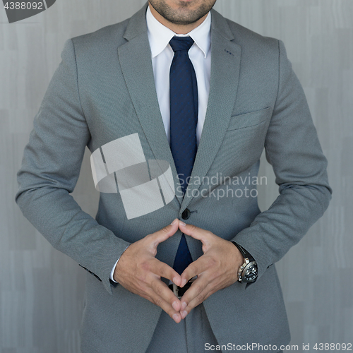 Image of Torso of anonymous businessman standing with hands in lowered steeple wearing beautiful fashionable classic grey suit, white shirt and blue tie.